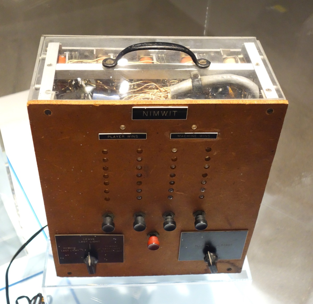 A wooden cabinet with a clear top showing valves and wiring.
                  A plate on the front reads NIMWIT, and two columns of lamps
                  beneath it are labelled PLAYER WINS and MACHINE WINS.
